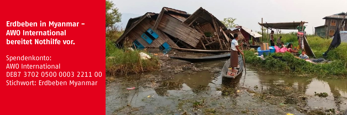 Das Bild zeigt ein eingestürztes Haus, das im Wasser liegt. Am Rand steht das Spendenkonto von AWO International. Copyrights (c) Harmony for Nexus Development 